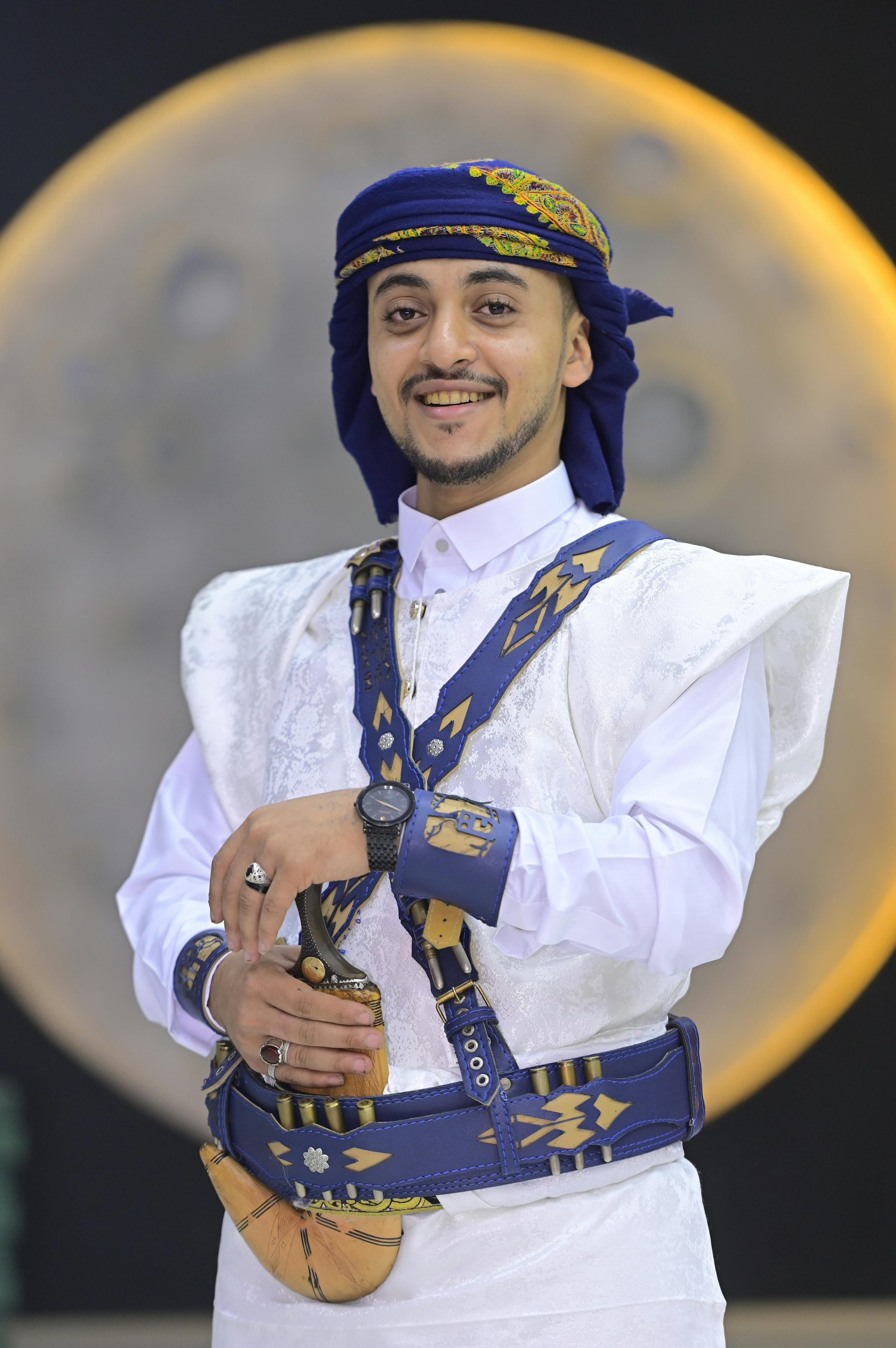 Smiling man in traditional Middle Eastern attire posing for a portrait with a moonlit background.